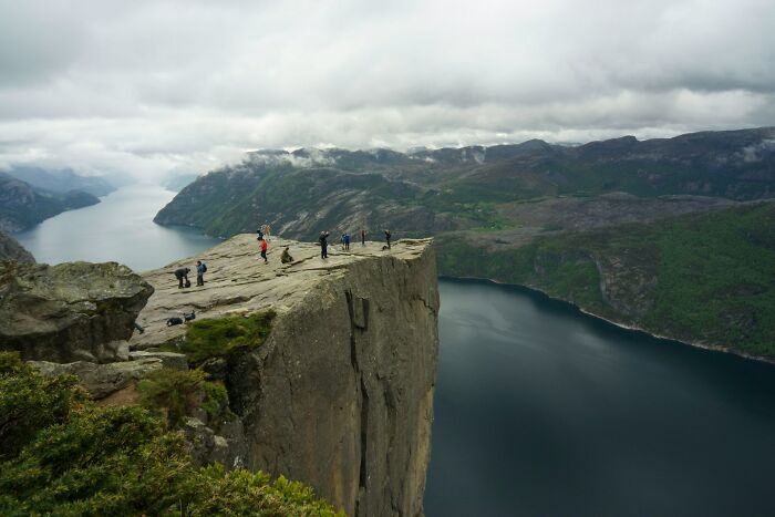 Cliff edge overlooking fjord with people standing and walking, highlighting almost hard to believe ways people died.