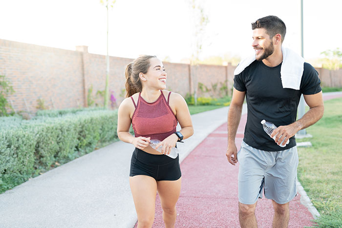 Man and woman running outdoors during the day, smiling and holding water bottles after exercise session.