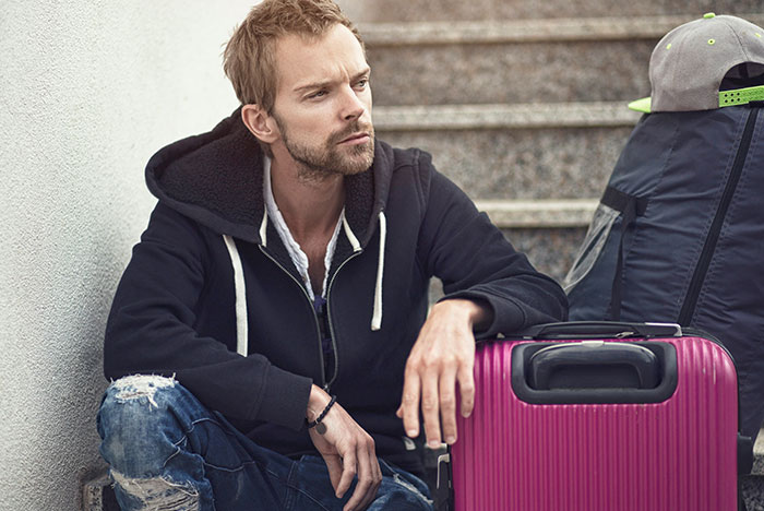Man sitting on stairs looking distressed with luggage nearby, reflecting wife&rsquo;s reaction to husband attending sister&rsquo;s baby shower.