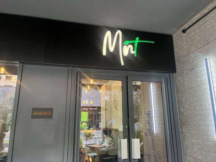 Entrance of Mint caf&eacute; with glass doors and a neon sign, highlighting caf&eacute; rules amid allergic customer controversy.