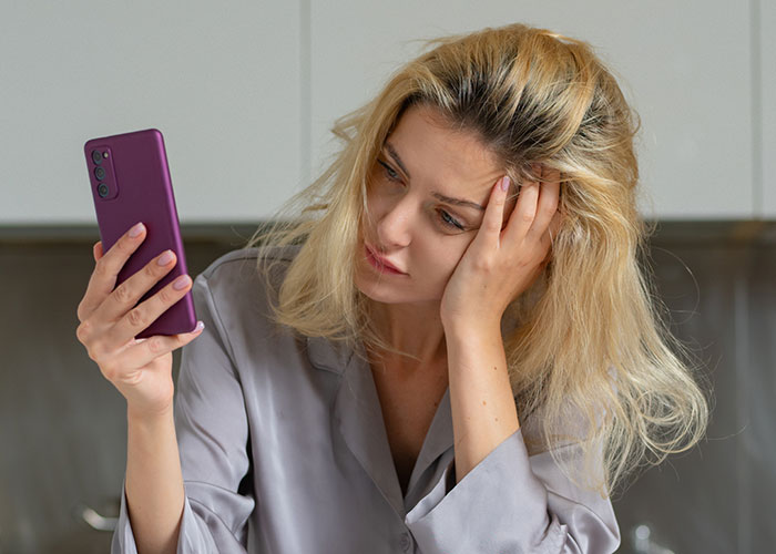 Woman looking worried and stressed while holding a smartphone, reflecting on petty drama affecting marriage and job concerns.