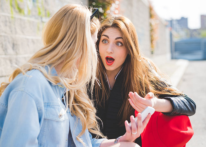 Two women outside, one showing surprise and concern, depicting relationship drama and worries about job impact.