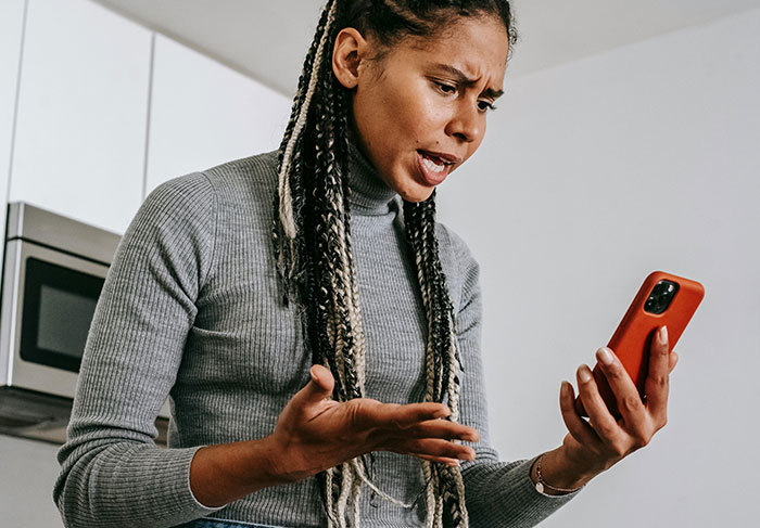 Woman with braided hair expressing frustration while looking at phone, illustrating man expects wife to rescue him after missing flight.