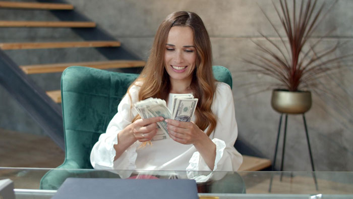 Woman counting money at a desk, smiling confidently, illustrating wife turned mean once got money concept.