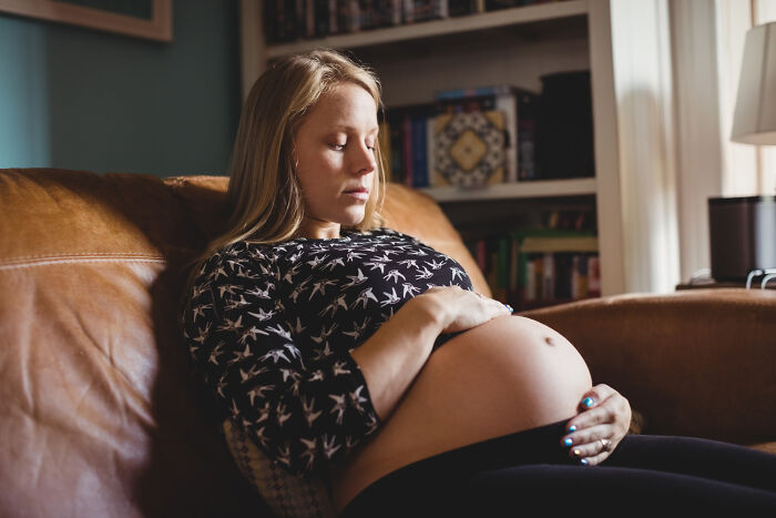 Pregnant woman sitting on a couch, looking thoughtful, depicting emotions related to toxic man and romantic conflicts.