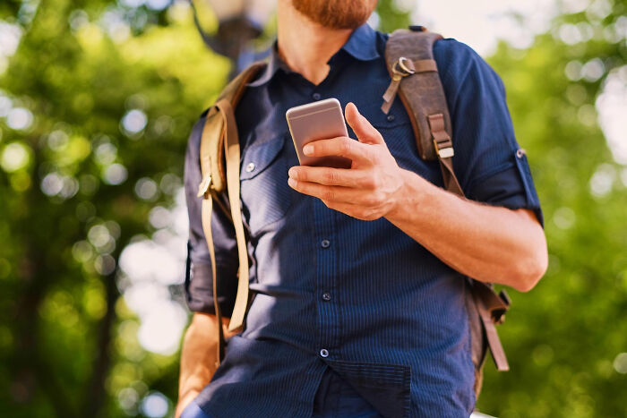Man wearing backpack outdoors, holding smartphone, representing toxic man romantically messing with two women.