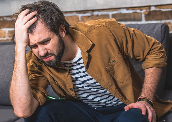 Man sitting on couch holding his head in pain, illustrating husband with a real problem needing an exit plan. Man sitting on couch holding his head in pain, illustrating husband with a real problem needing an exit plan.