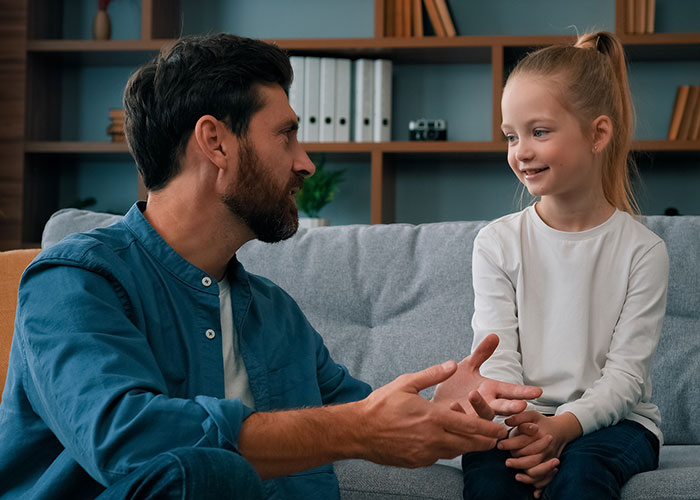 Man and young girl sitting on a couch in a nursery, engaged in a heartfelt conversation about family challenges. Man and young girl sitting on a couch in a nursery, engaged in a heartfelt conversation about family challenges.