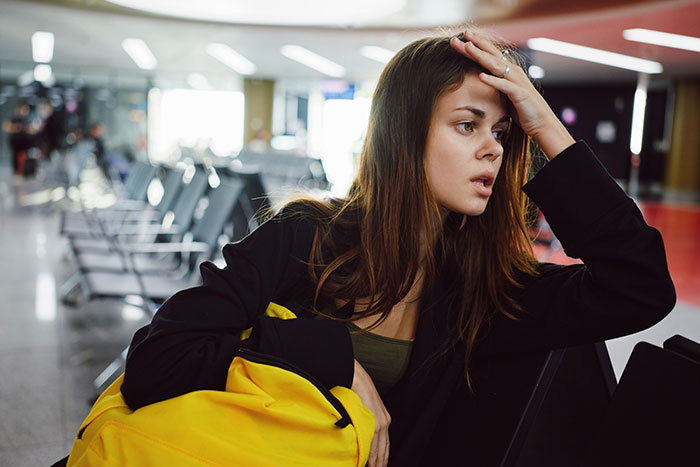 Young woman looking distressed holding yellow purse, sitting in a public waiting area, reflecting on a friendship fallout.