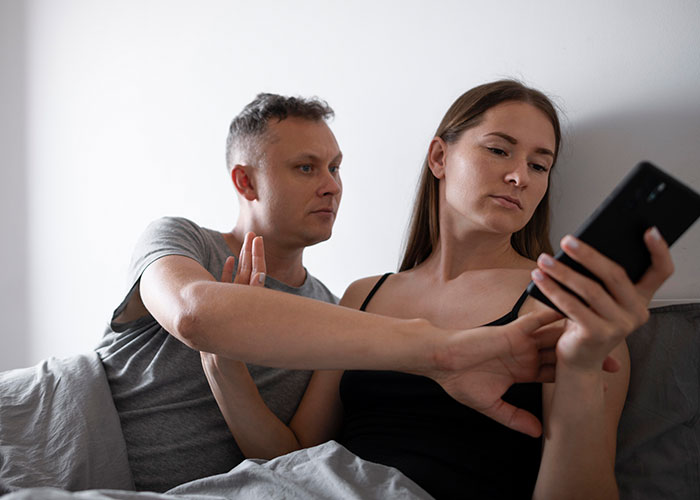 Woman looks upset holding phone while man tries to talk, illustrating woman learns she was her husband's second choice. Woman looks upset holding phone while man tries to talk, illustrating woman learns she was her husband's second choice.