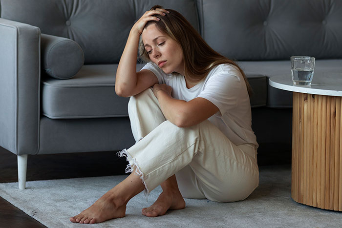 A distressed woman sitting on the floor, holding her head, depicting a woman&rsquo;s world crumbling after dark marriage secrets.