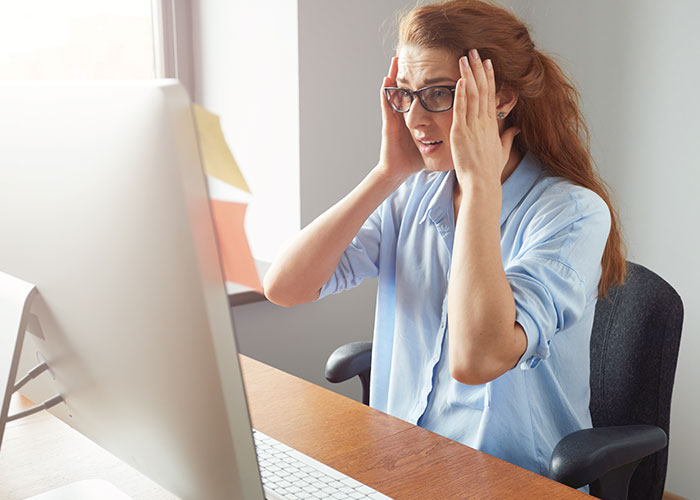 Woman at work looking shocked while setting up WIC profile, discovering husband's affair baby news on computer.