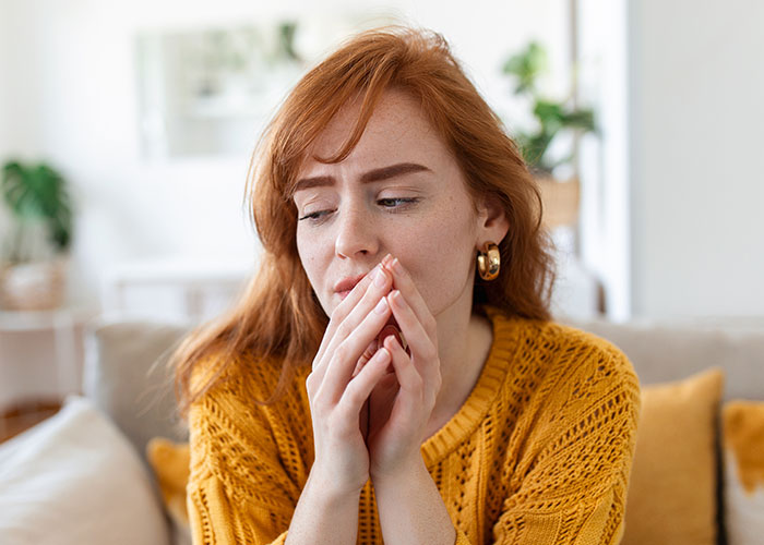 Woman in a yellow sweater looking worried and thoughtful while sitting indoors, representing affair baby discovery and WIC profile setup.