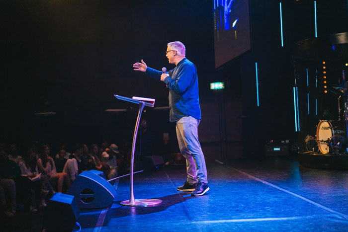Comedian performing on stage during a stand-up show with an engaged audience in a dimly lit venue. Comedian performing on stage during a stand-up show with an engaged audience in a dimly lit venue.
