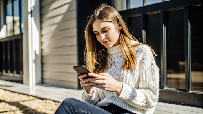 Young woman outdoors using smartphone, focused on dating app, considering tests to spot red flags on dates.