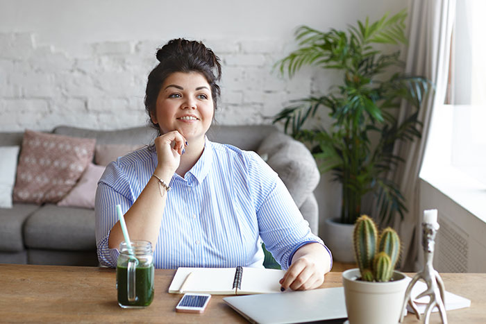 Overweight woman sitting at desk with notebook and laptop, reflecting on new manager comments about fitness to see clients.