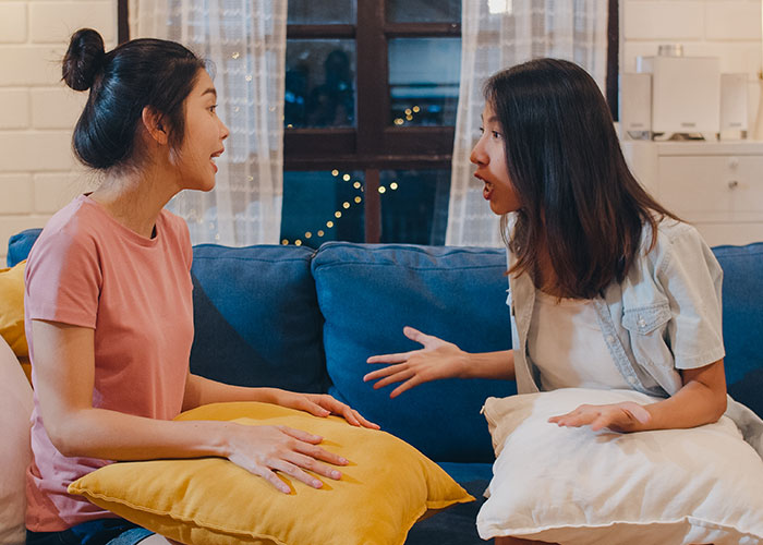 Two women sitting on a sofa engaged in a tense conversation, reflecting a woman forbidding BIL from talking to her.