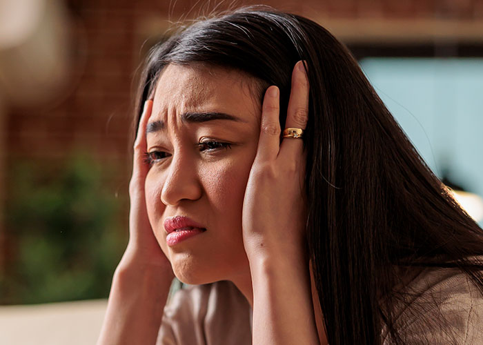 Woman looking frustrated and stressed, holding her head in her hands, depicting tension with brother-in-law and nephew issues