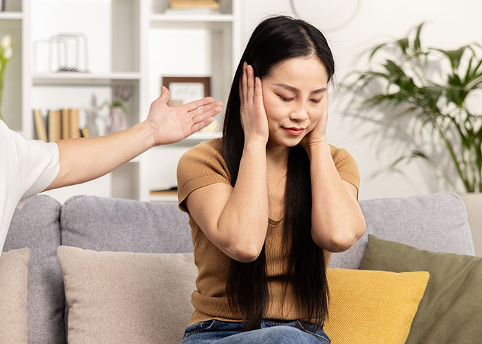 Asian woman covering ears while man nearby gestures, illustrating tension as woman forbids BIL from talking to her.