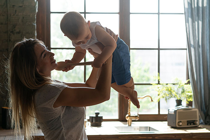 Woman holding baby near window, reflecting on artificial insemination and motherhood plans in a cozy home setting.
