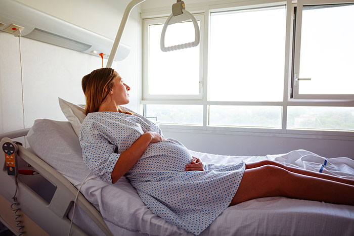 Pregnant woman in hospital gown lying on bed, contemplating motherhood and artificial insemination plans.