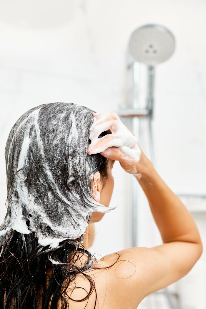 Person washing hair with shampoo foam in shower illustrating everyday things that humble adults.