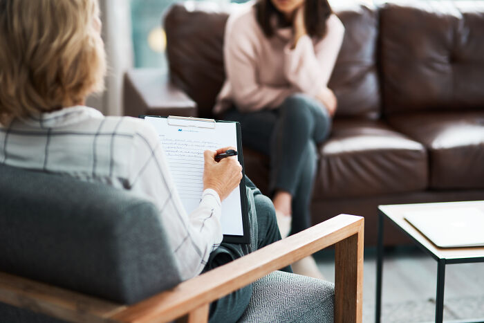 Therapist taking notes during a session with a woman on a couch, illustrating out-of-touch conversation moments.