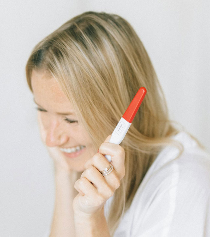 Woman holding a pregnancy test with a smile, capturing a dramatic pregnancy reveal moment. Woman holding a pregnancy test with a smile, capturing a dramatic pregnancy reveal moment.