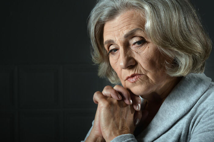Elderly woman with a somber expression reflecting on diet and food-shaming concerns in a dark setting.