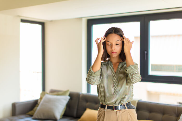 Tense woman in casual clothes standing in living room, showing frustration related to diet-obsessed mom and food shaming.