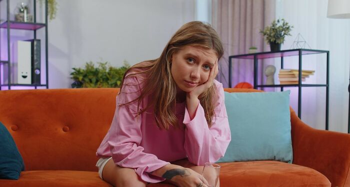 Young woman looking upset on orange couch, illustrating diet-obsessed mom food-shaming daughter conflict at home.