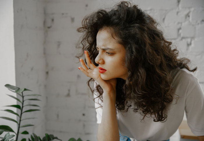 Woman with curly hair and red lipstick looking upset and frustrated in a bright room with white brick walls.