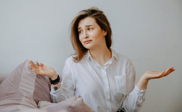 Woman in white shirt shrugging with a frustrated expression, illustrating conflict during homeowners party dispute.