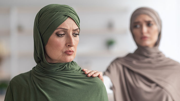 Two women wearing hijabs, one comforting the other who looks upset, highlighting a tense or unfair situation. Two women wearing hijabs, one comforting the other who looks upset, highlighting a tense or unfair situation.