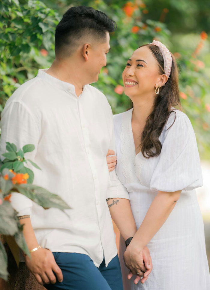 Couple holding hands and smiling outdoors, highlighting man lashing out at fianc&eacute;e over family dress shopping issue.