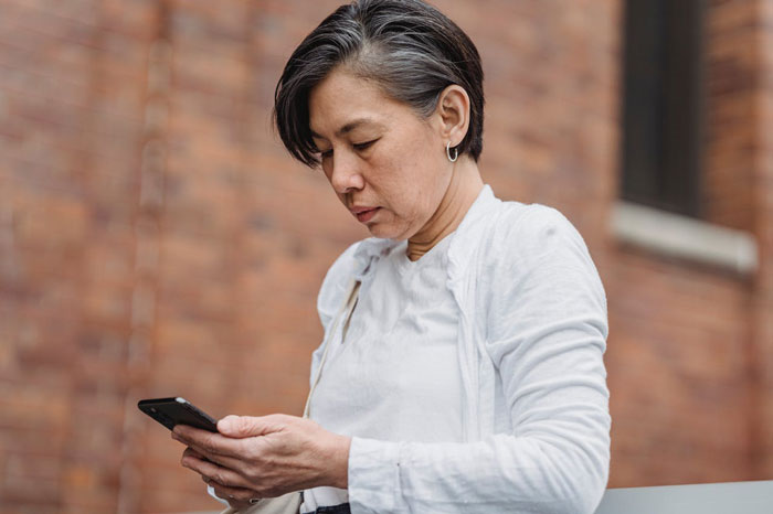 Middle-aged woman looking upset while checking her phone, reflecting tension related to dress shopping with family.