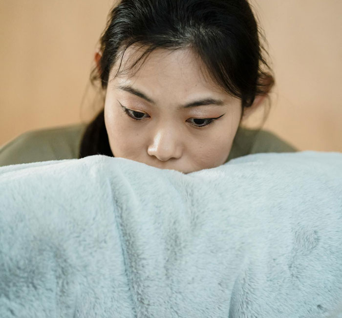 Young woman looking upset and contemplative, resting on a soft blanket, reflecting on dress shopping conflict with family.