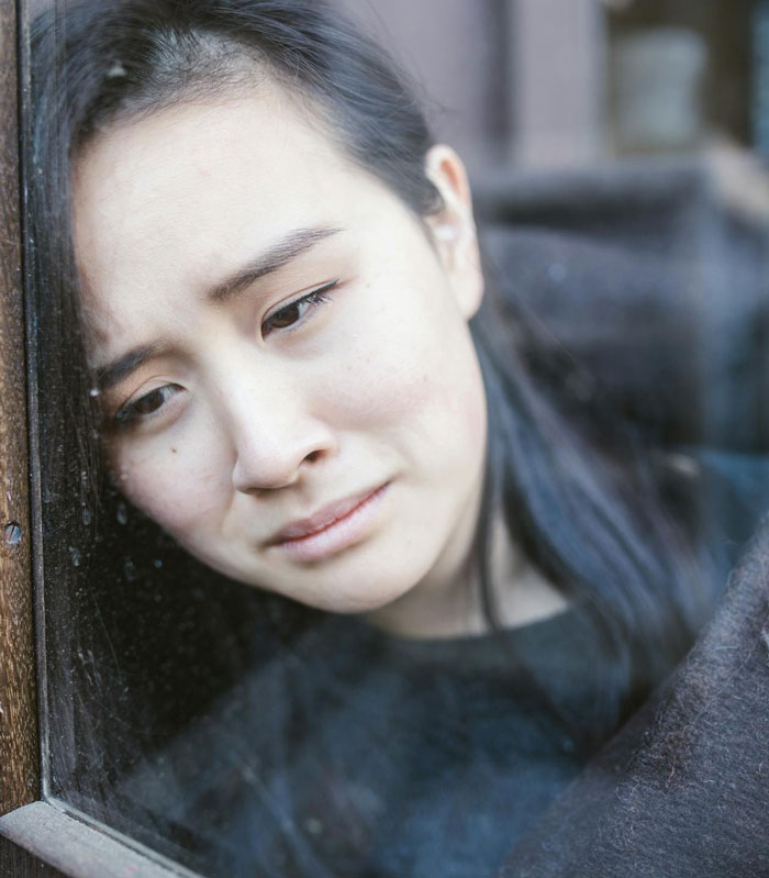 Sad woman looking out of window upset after man lashes out at fianc&eacute;e over family dress shopping issue