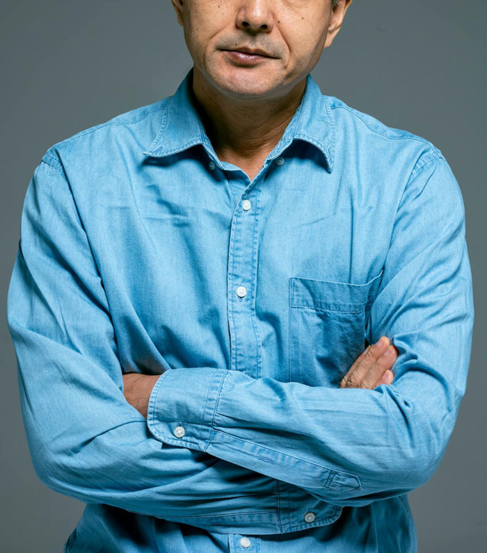 Man with arms crossed, wearing a blue shirt, showing frustration related to family dress shopping without fianc&eacute;e.