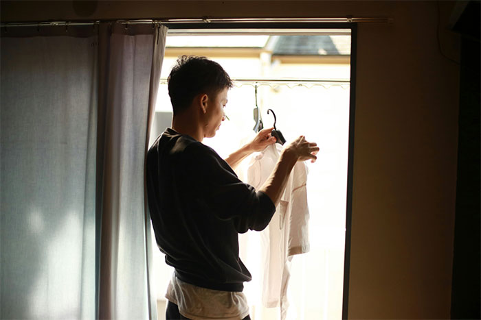 Man standing by a window, holding a shirt on a hanger, illustrating living with men experiences shared by women.