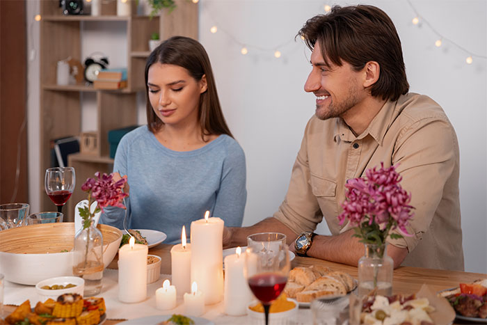 A woman and man sitting at a dining table with food, candles, and flowers, reflecting on living with men.