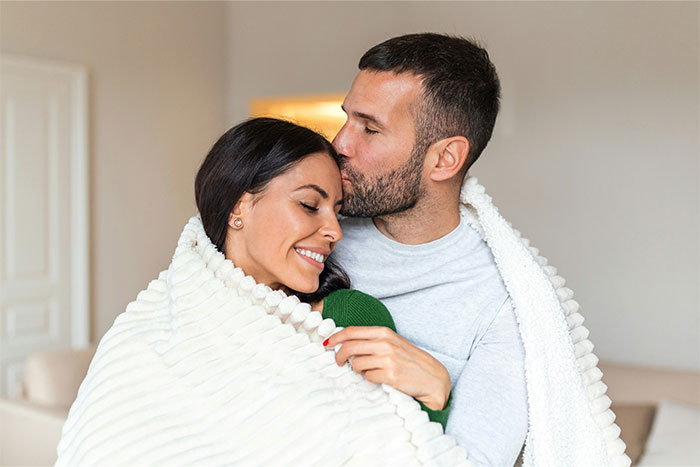 Happy couple wrapped in a white blanket sharing a tender moment, reflecting women's revelations after living with men.