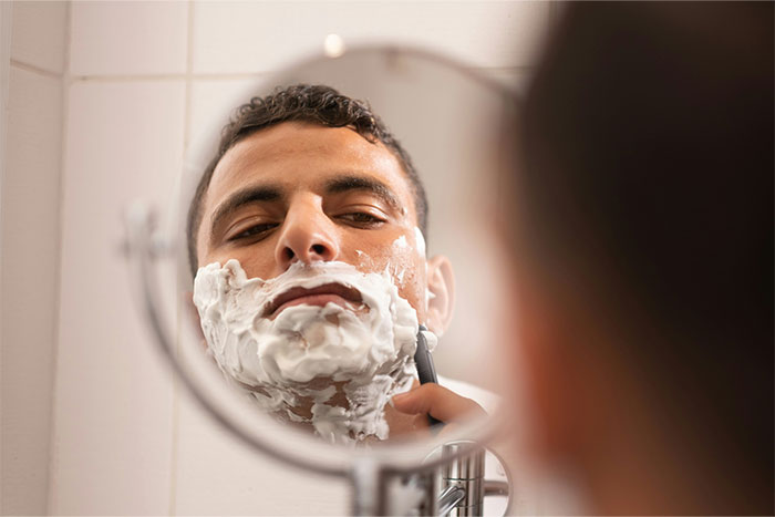Man shaving in bathroom mirror, illustrating common daily habits of men living with women.