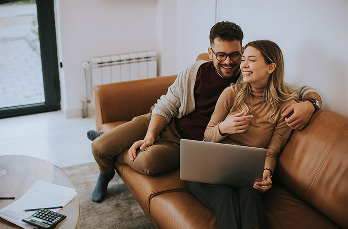 Young couple sharing a laptop on a couch, smiling and relaxed, highlighting women’s revelations after living with men.