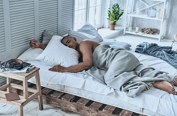 Man sleeping on bed wrapped in gray blanket in a bright bedroom, illustrating life living with men revelations.