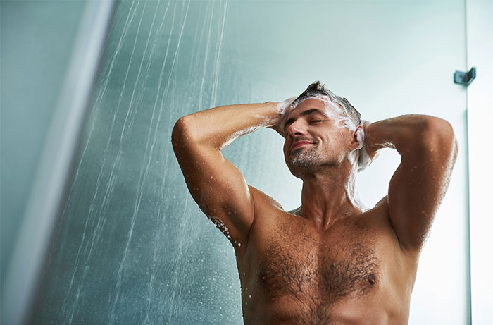 Man washing hair in shower, relaxing under running water, illustrating daily life living with men insights shared by women.