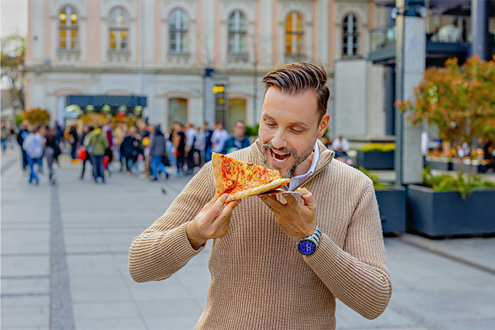 Man enjoying a slice of pizza outdoors, illustrating casual moments in everyday life and shared living experiences.