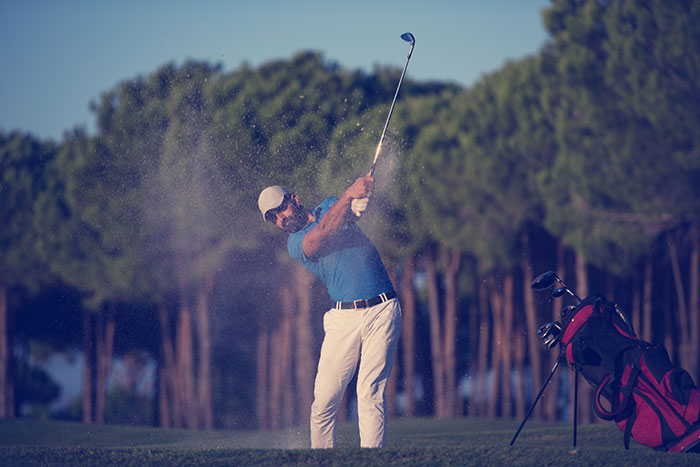 Man hitting golf ball from sand trap on course, illustrating rage-baits from women to ruin a man’s day.