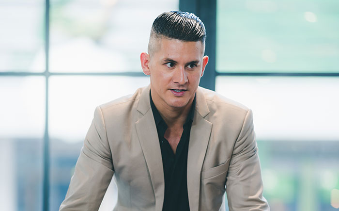 Man in beige blazer with slicked-back hair, appearing serious and contemplative in a modern office setting, rage-baits concept.