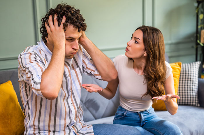 A woman angrily confronts a frustrated man on a couch, illustrating rage-baits that ruin a man's day.